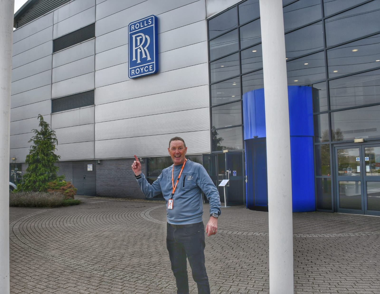 Team arriving at Rolls Royce Derby campus - NexGen Portable Staging & Dancefloors There's a particular feeling when you return to a customer after seven years. Not as a stranger with a brochure. Not as a supplier chasing renewal. But as a partner they've chosen to trust—again. This March, our NexGen team headed back to Rolls Royce's Derby campus. Back in 2017, we installed their first portable staging system Man wearing a blue jacket with an orange lanyard stands outside a Rolls-Royce building, pointing upward with a smile.