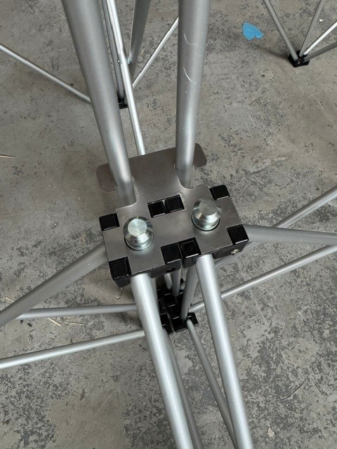 NexGen Riser Leg Link Clamp (Dual) 6 Pack This spare parts connects multi riser legs together of different heights, for use with differing height riser legs where the deck platforms cannot be aligned. Such as a lower step or tier setup. Place the link clamp around the two taller of the two riser legs, and Metal tripod joint with a square metal plate and bolts connecting aluminum tubes on a concrete floor.
