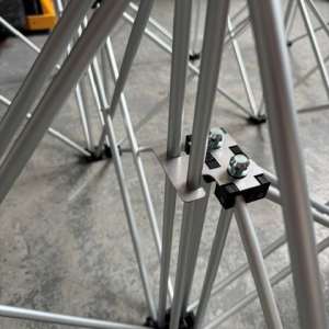 Close-up of gray metal tubing joined by a small black connector plate with two bolts, forming a tubular frame on a concrete floor.