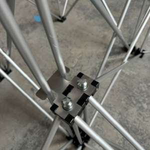 Close-up of a metal scaffold truss joint with a square plate secured by bolts, connecting silver tubes.