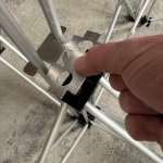 Close-up of a hand aligning a perforated metal connector with a scaffolding frame for assembly