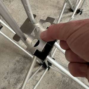 Close-up of a hand aligning a perforated metal connector with a scaffolding frame for assembly