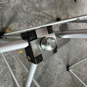 Close-up of a metal joint with a large bolt and black plastic spacers on a gray folding frame, on a concrete floor.
