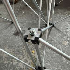 Close-up of a metal scaffold joint with a bolt and clamp on a concrete floor coasted by cross braces and rails, mid-assembly piece.