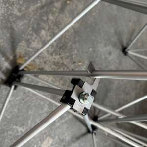 Close-up of a metal frame joint with a bolt and black clamps on a concrete floor.