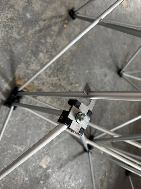 NexGen Riser Leg Link Clamp (Single) 6 Pack This spare parts connects riser legs together of different heights, for use with differing height riser legs where the deck platforms cannot be aligned. Such as a lower step or tier setup. Place the link clamp around the taller of the two riser legs, and over the Close-up of a metal frame joint with a bolt and black clamps on a concrete floor.